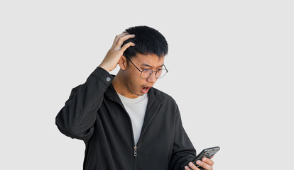 Young Asian man wearing black coat is excited and surprised by notification on his cell phone, isolated on white background. Man is surprised by message he received on his smartphone. Shock face