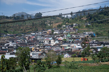A panoramic view of a densely populated village nestled on terraced hillsides, with mountains and...