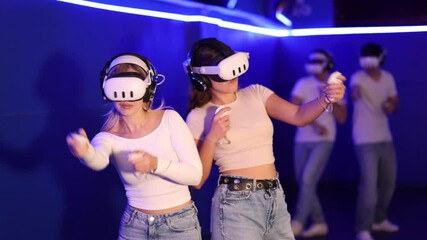 Two girls wearing virtual reality glasses participate in game with opponents. They compete two-on-two with male friends while playing in parallel virtual world. - Powered by Adobe