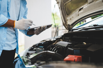 A mechanic wearing gloves inspects a car engine and keeps a checklist, focusing on maintenance and repair for the safety, reliability and optimum performance of the car in the auto repair shop.