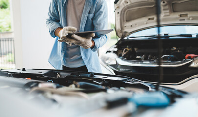 A mechanic wearing gloves inspects a car engine and keeps a checklist, focusing on maintenance and repair for the safety, reliability and optimum performance of the car in the auto repair shop.