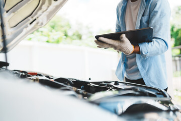 A mechanic wearing gloves inspects a car engine and keeps a checklist, focusing on maintenance and repair for the safety, reliability and optimum performance of the car in the auto repair shop.