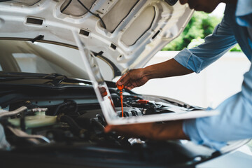 Mechanic checking engine oil using laptop to thoroughly inspect engine Focuses on maintenance and...