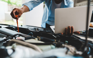 Mechanic checking engine oil using laptop to thoroughly inspect engine Focuses on maintenance and...