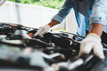 A professional mechanic wearing gloves uses wrenches to repair a car engine under the open hood,...