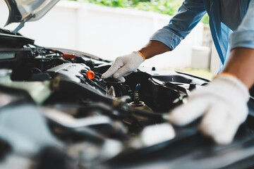 A professional mechanic wearing gloves uses wrenches to repair a car engine under the open hood,...