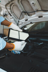 Obraz premium A gloved mechanic inspects and changes a car's air filter under an open hood, performing essential maintenance to ensure reliable performance and efficiency of the car in an auto repair shop.