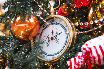 The clock hands on the dial show 12 o'clock. Golden retro clock on a Christmas tree. Beautiful...