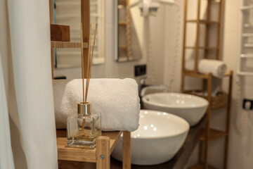 Minimalist bathroom interior with white towel, aroma diffuser, and modern ceramic sinks. Wooden shelving and soft lighting create a spa-like atmosphere