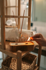 A cozy bathroom moment as a person lights a handmade wooden candle with two wicks, surrounded by a...