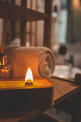 A handmade wooden candle with twin flames burning brightly on a bamboo shelf in a spa-style bathroom, accompanied by a rolled towel and glass diffuser, creating a serene and cozy atmosphere