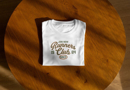 Mockup of  folded white t-shirt is placed on a round wooden table.