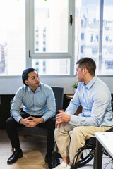 Two young businessmen are having a conversation in a modern coworking office, one of them using a...