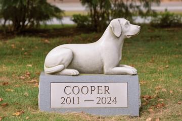 Gravestone with dog stone sculpture in a peaceful cemetery. Memorial for a beloved pet and pet loss remembrance