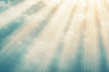 Sunlight streams through softly textured clouds, casting radiant rays across a serene blue sky.