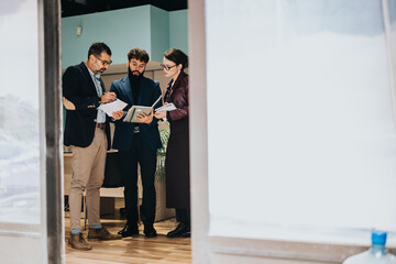 Three business people discussing work-related documents in a modern office environment. The team...