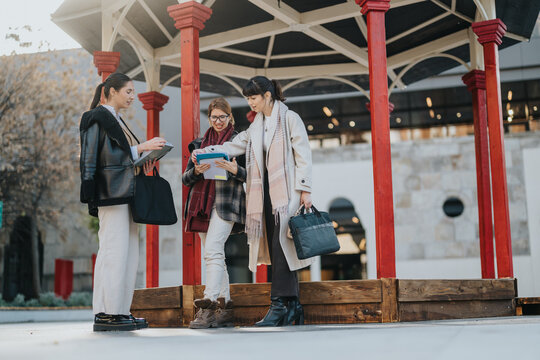 A group of professional women, wearing formal attire, working together in a public outdoor area, sharing ideas and reviewing documents, emphasizing teamwork, collaboration, and modern business - Powered by Adobe