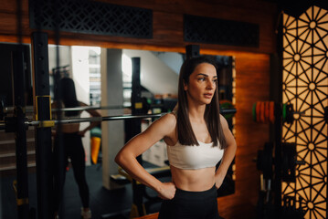 Determined sportswoman posing with hands on hips in gym after workout