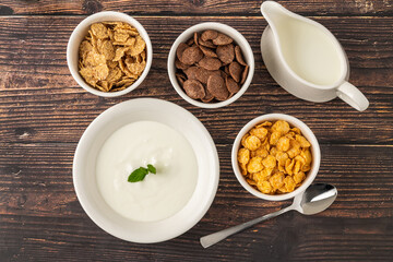 Assorted cereals with yogurt and milk on rustic wooden table