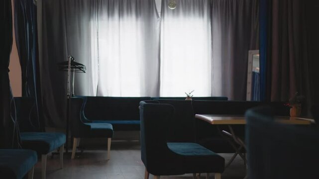 Interior of cozy caf with velvet blue seating and wooden tables. Large window with soft natural light filtering through curtains. Calm and peaceful atmosphere enhanced by minimalist d cor