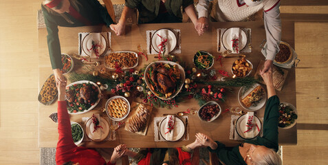 Holding hands, praying and people in home, dinner or gratitude for food on Christmas or celebration. Above, faith and prayer for feast on holiday, group and family in house for thanksgiving and night