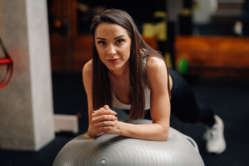 Determined sportswoman performing plank exercise on fitness ball in gym