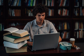 Focused student working on laptop in library with books and lunch