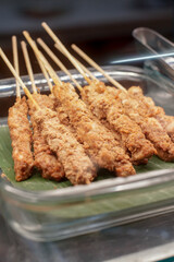 Close-up of Indonesian spiced chicken satay skewers served on banana leaf in a glass tray. Traditional Southeast Asian grilled street food.
