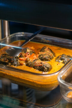 Close-up of Indonesian buntil made from cassava leaves filled with seasoned grated coconut, cooked in spicy coconut milk, served hot in a food warmer.