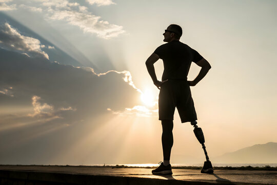 Silhouette of an amputee standing confidently against a warm, sunny sky, symbolizing resilience and strength near the water.