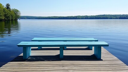 Two light-blue benches sit on a wooden dock overlooking a tranquil lake, surrounded by lush greenery under a clear sky