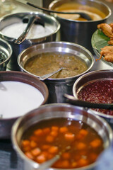 Various traditional Indonesian desserts such as kolak, bubur sumsum, and sweet mung bean porridge served in stainless steel bowls at a local market food stall.