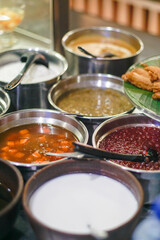 Various traditional Indonesian desserts such as kolak, bubur sumsum, and sweet mung bean porridge served in stainless steel bowls at a local market food stall.