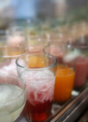 Close-up of colorful Indonesian cold drinks, including coconut and syrup, in tall glasses.