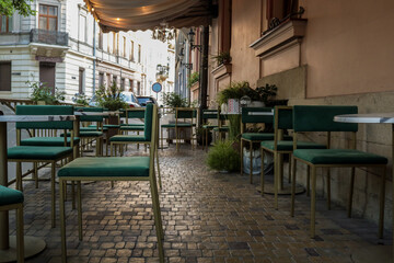 Outdoor seating area of a stylish café with green velvet chairs, white tables, and potted plants...