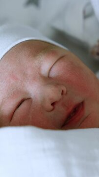 Adorable newborn Caucasian child wakes up and makes faces. Baby opens one eye and falls asleep again. Close up. Vertical video