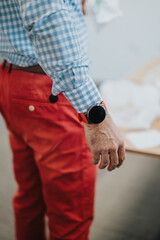 Naklejka premium Close-up of a professional wearing stylish business casual clothing, a checkered shirt, red trousers, and a smart watch, emphasizing focus and sophistication in a workplace setting.