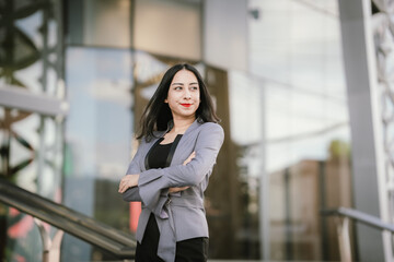 A confident woman in a gray blazer stands tall in an urban setting, showcasing elegance, strength,...