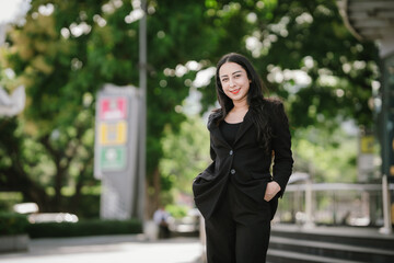 A confident, stylish woman in a black blazer walks through the city with coffee and smartphone in...
