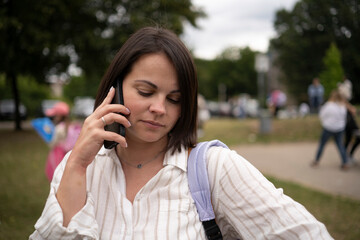 Focused woman on a phone call in summer city street with people passing by. Concept: digital connection, real-time decisions, city rhythm, independence.