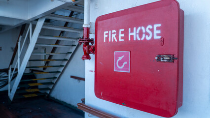 Red fire hose box on a passenger ship deck with stairs in the background