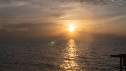 Fototapeta premium Sunrise over a calm ocean with a bright sunburst and reflection on the water