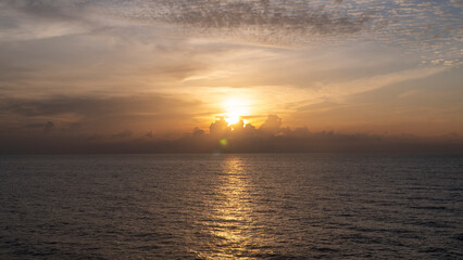 Fototapeta premium Sunrise over the ocean with the sun partially obscured by clouds, casting a golden reflection