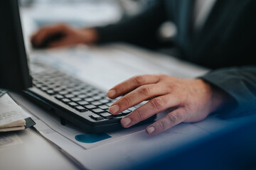 Focused hand typing on a keyboard with official documents on the desk