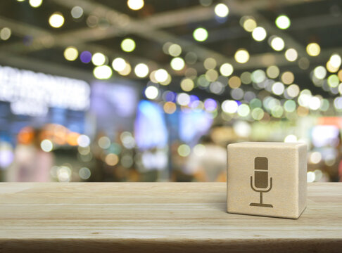 Microphone flat icon on wood block cube on wooden table over blur light and shadow of shopping mall, Business communication concept