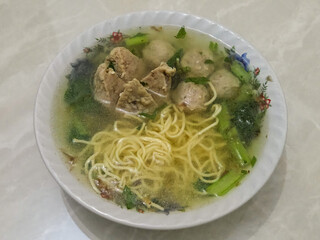 Traditional bowl of yellow noodle soup with vegetables and meatballs served on a white background in a homemade setting, Bakso Meatballs
