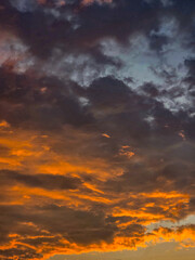 Dramatic evening sky with dark purple clouds and intense orange sunlight during sunset, showing vibrant twilight colors