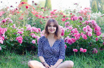 Beautiful young woman in a polka dot dress with roses, in a park on a sunny day