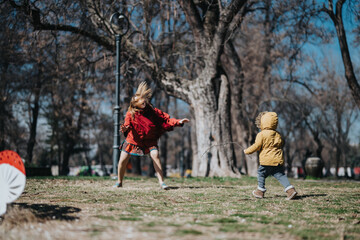 Fototapeta premium Two children engage in playful activities under the sunny sky in a park with trees. The scene showcases outdoor fun and happiness.