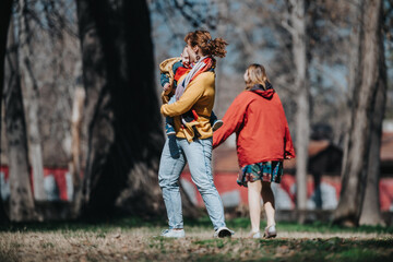 Fototapeta premium Woman holding and carrying a small child in her arms while walking in a natural park setting with trees, accompanied by another woman.